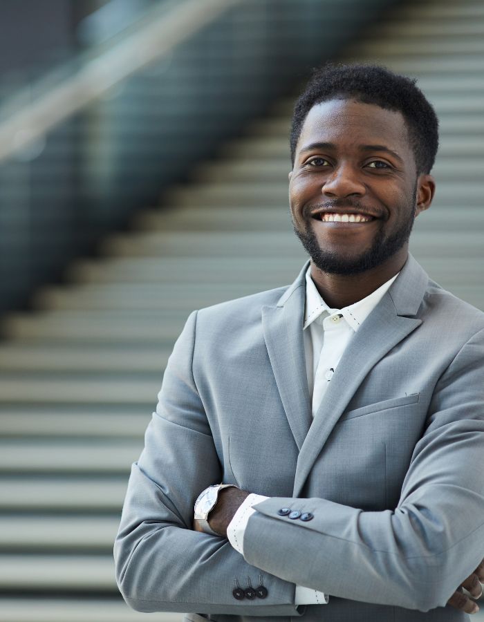 Young black man wearing a gray suit and smiling while standing on concrete stairs