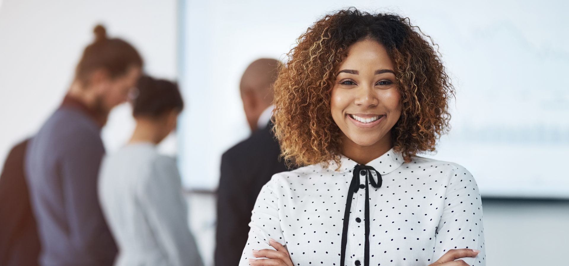 Young Black woman with curly brown hair wearing a white and black polka dot shirt