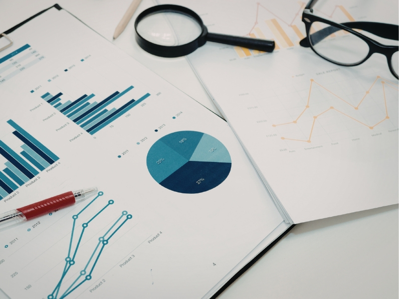 Printed financial graphs next to magnifying glass and eye glasses