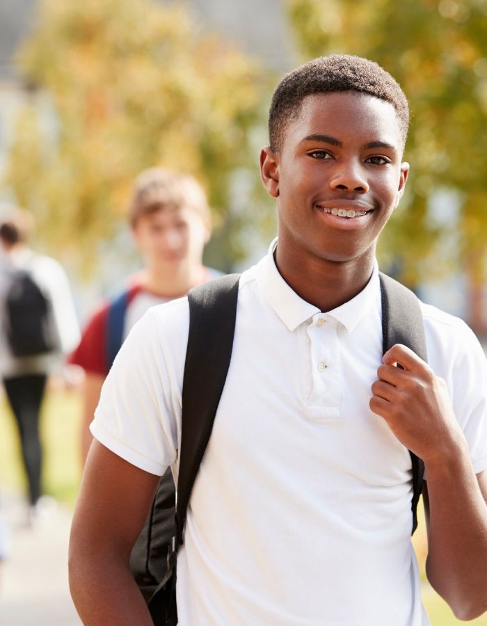 Black male high school student wearing white polo shirt carrying a black backpack