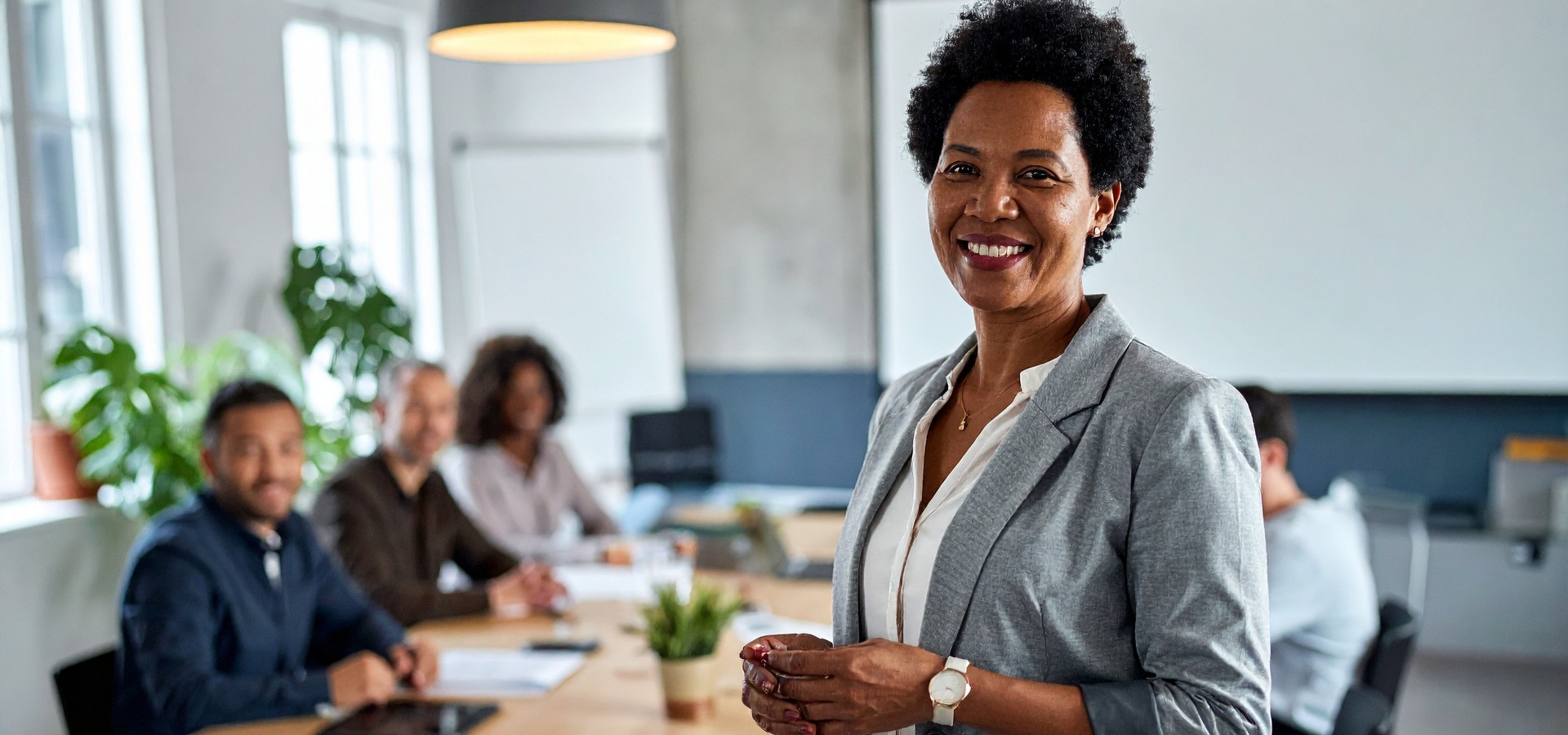 Black woman smiling while her team sits at table behind her