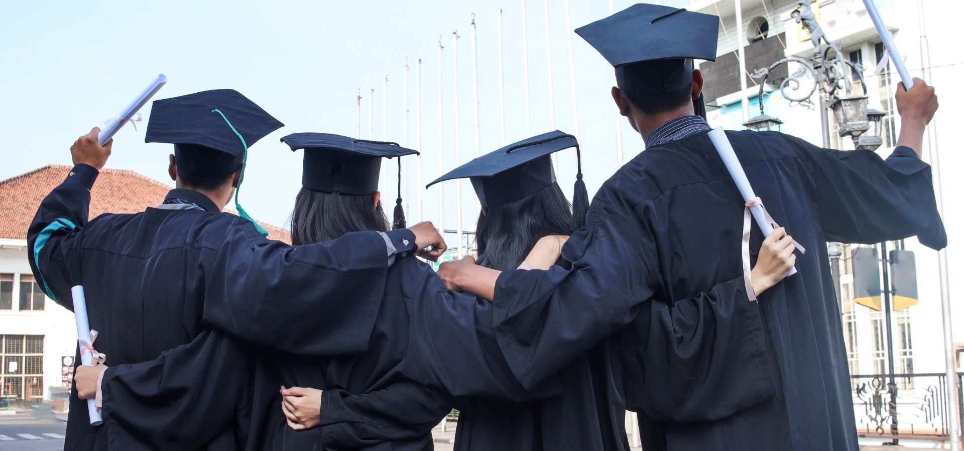 Group of four graduates wearing black caps and gowns facing away from camera